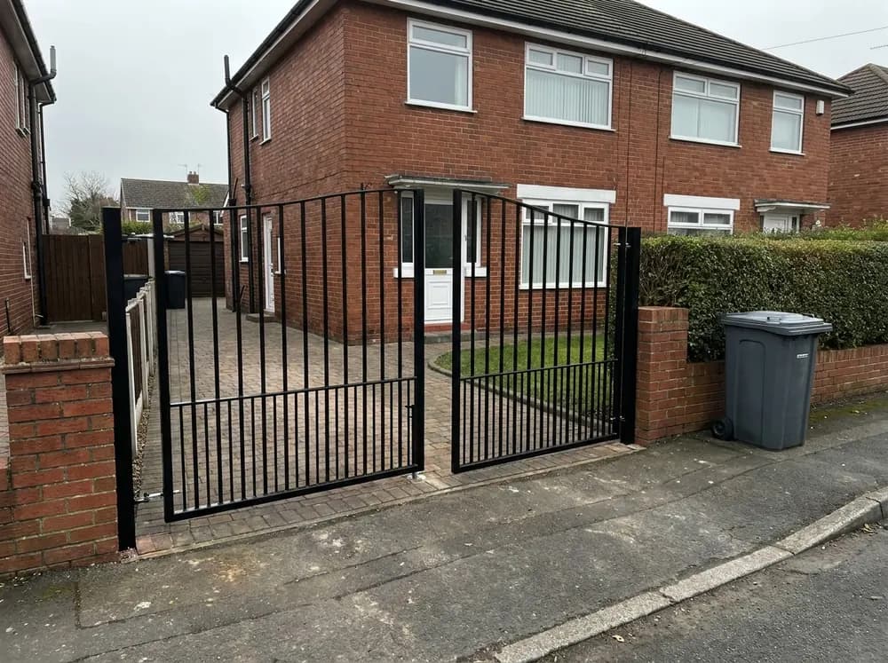 Black painted iron double gates standing part open on a block paved driveway