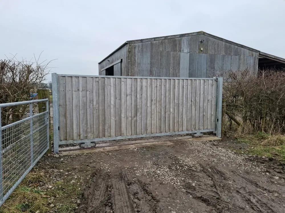 A timber close board sliding gate running on a ground track at a farm entrance