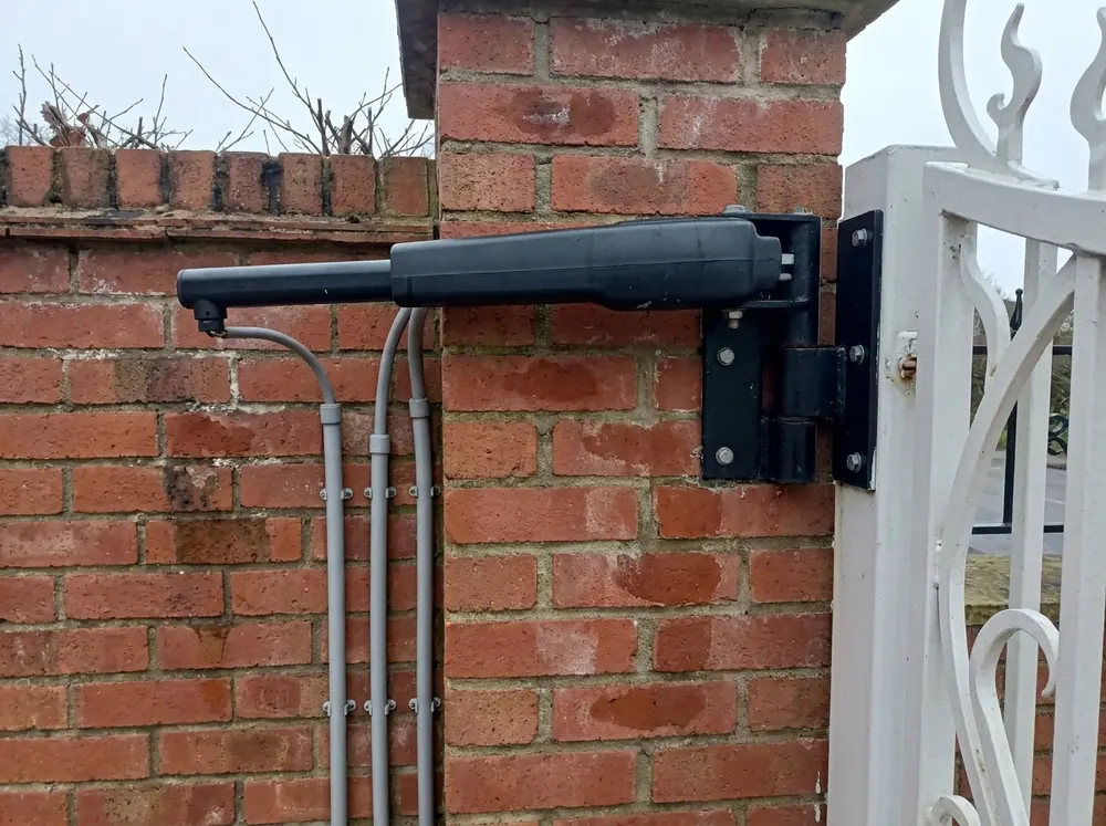 Close detail of an electric gate motor and hinge mounted on a red brick pillar with cabling in conduit